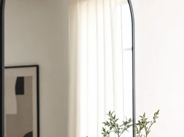 Close view of a clean thin matte black arched mirror frame above a wood console