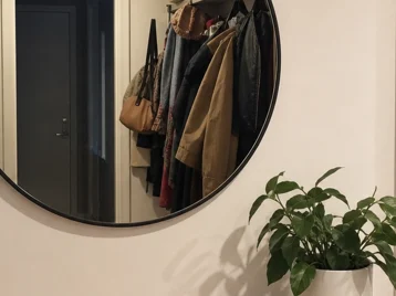 Round mirror reflecting a dark doorway, coats, bags, and a harsh ceiling light