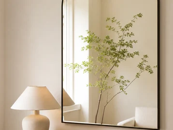 Arched mirror positioned to reflect soft window light and a calm leafy branch