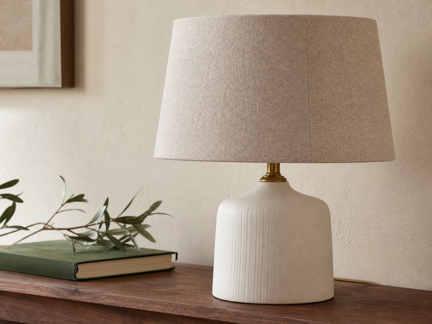 Close view of a matte ceramic lamp with clean brass neck and woven linen shade