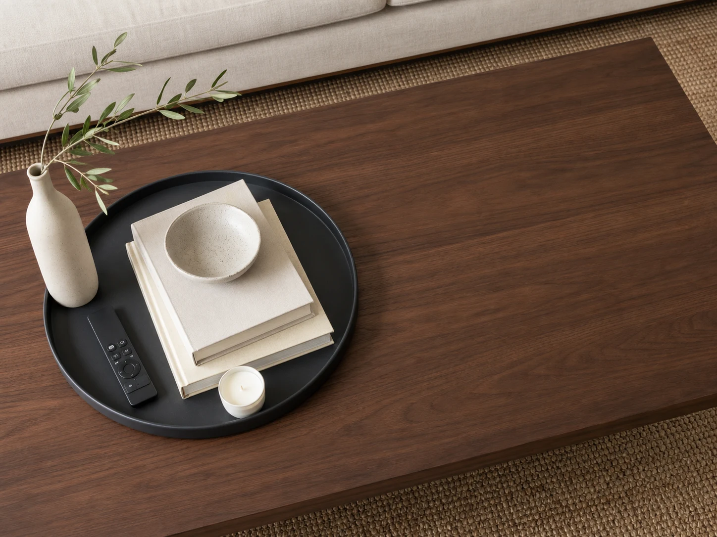 Remote, books, bowl, candle, and vase grouped inside a charcoal tray on a clear walnut table